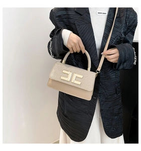 Gros plan du sac beige avec texture à paillettes et détail du logo doré chic