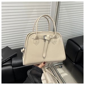 Close-up of cream beige handbag with top handle and decorative buckle strap detail
