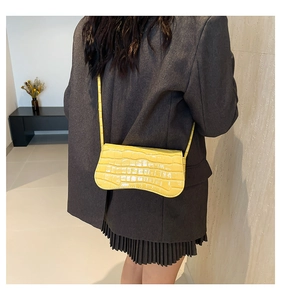 Detail of yellow crocodile-embossed handbag with iconic curved base worn by a model