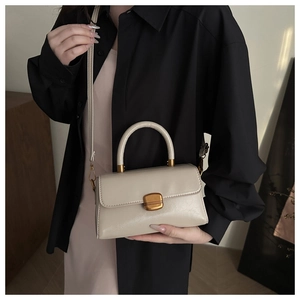 Close-up of minimalist cream leather handbag with gold metal clasp and top handle