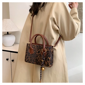 Detail of leopard print crossbody bag with gold bell charm and brown leather straps