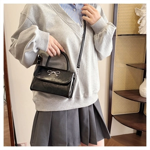 Detail of black leather crossbody bag with silver bow accent on model in school style outfit
