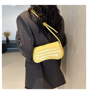 Detail of yellow crocodile embossed shoulder bag with unique knot strap on a model