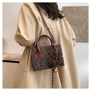 Detail of leopard print tote bag with brown leather handles and a woven bell charm