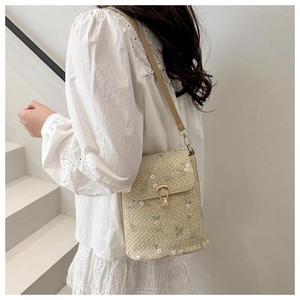 Détail de broderie florale vintage et boucle dorée sur un sac bandoulière tissé