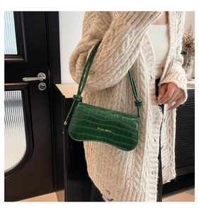Detailed view of dark green crocodile texture shoulder bag worn with a knit cardigan