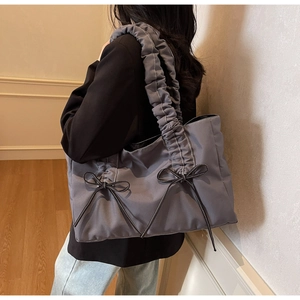 Detail of grey nylon tote bag featuring ruffled straps and black leather bow accents