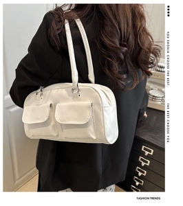 Detail view of a white glossy shoulder bag with dual front pockets worn by a model