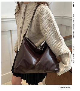 Deep brown oversized tote bag in glossy faux leather worn by a model in warm setting