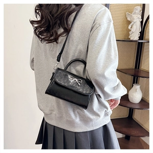 Detail of black glossy square bag with silver metal bow and detachable shoulder strap