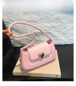Dettaglio di una borsa sottobraccio rosa con fibbia a cuore dorata su sfondo materico