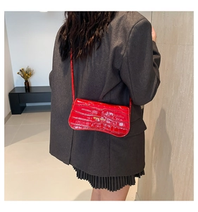 Detail of red crocodile pattern shoulder bag with gold logo on gray blazer outfit