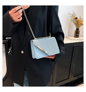 Close-up of light blue crossbody bag with woven texture flap and gold chain strap