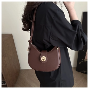 Detail of a brown hobo bag with a gold round clasp shown on model's shoulder