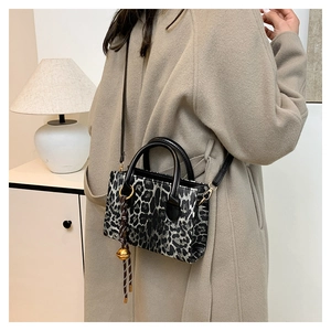 Detail of leopard print mini crossbody bag with gold bell charm and woven strap
