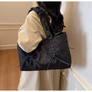Close-up of pleated shoulder strap and white stitching on a black nylon tote bag