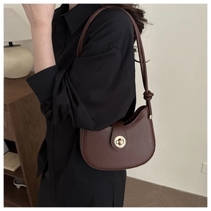 Détail d'un sac besace en cuir mat marron foncé avec fermoir doré et bandoulière nouée