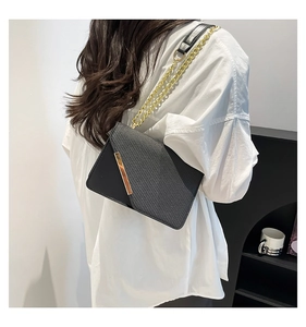 Detail of woven texture flap and gold metal bar on black crossbody envelope bag