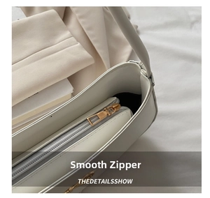 Close-up of a smooth gold metal zipper on a premium white faux leather underarm bag