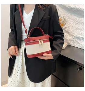 Detail of canvas vanity bag with red leather trim and double gold zippers on a shelf