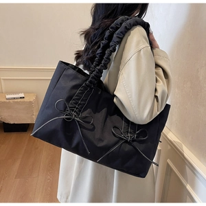 Detail of black nylon tote bag featuring white bow accents and ruched shoulder strap