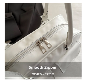 Detail shot of the smooth metal dual-zipper closure on a white vegan leather shoulder bag