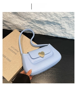 Dettaglio della borsa a spalla azzurra con chiusura a cuore dorata su sfondo bianco