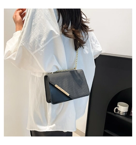 Detail of black crossbody bag featuring textured flap and elegant gold chain strap