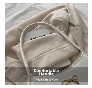 Detail of white baguette bag featuring a gold bow ornament on smooth matte texture