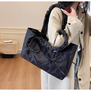 Detailed view of black nylon tote bag featuring gathered cloud handles and white bow stitching