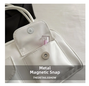 Detail of white leather tote bag featuring a silver magnetic snap closure on exterior pocket