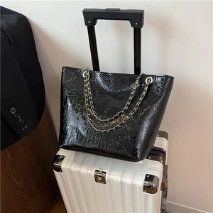Sac fourre-tout noir à motif crocodile avec poignées en chaîne dorée sur valise