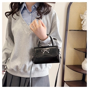 Detail of black patent leather square bag with silver bow buckle and sturdy handle