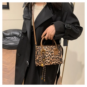 Detail view of leopard print handbag with woven strap charm and gold bell accessory