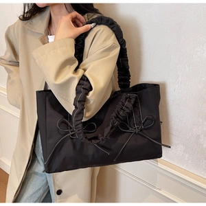 Macro view of black nylon tote bag featuring ruffled strap and white bow stitch details