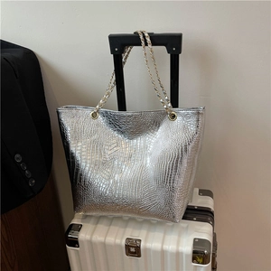 Sac cabas argenté motif crocodile avec bandoulière chaîne sur une valise blanche