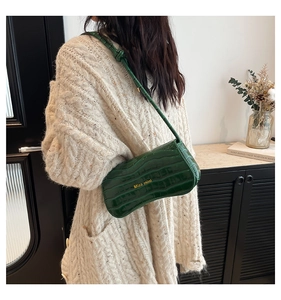 Close-up of green crocodile texture shoulder bag with gold lettering shown as underarm bag