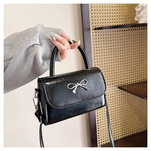 Detail of a black leather handbag with a polished silver metal bow and fine stitching