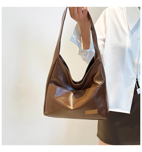 Close-up of brown PU leather tote bag with wide shoulder strap and front pocket detail