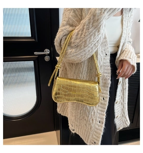 Detail of golden crocodile embossed shoulder bag with unique knotted strap and sleek texture