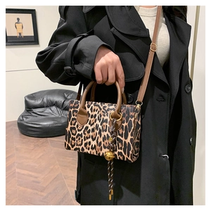 Detail of leopard print handbag featuring brown handles and a gold bell charm