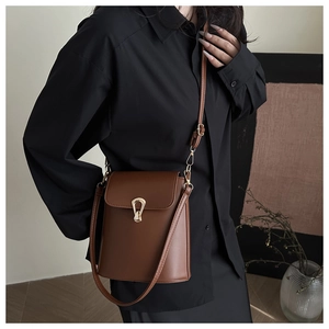 Detail of caramel leather bucket bag featuring a gold horseshoe buckle and adjustable strap