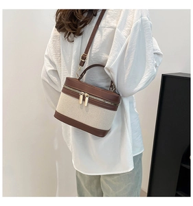 Detail of canvas bucket bag with brown leather trim and dual gold metal zippers