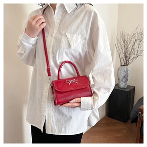 Detail of red glossy crossbody bag with silver bow buckle and adjustable strap