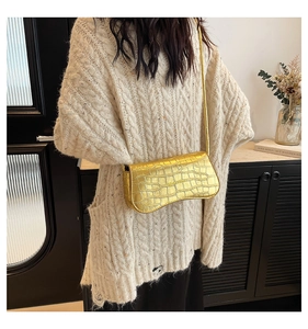 Detail of gold crocodile embossed shoulder bag worn with a knit sweater in a cozy room