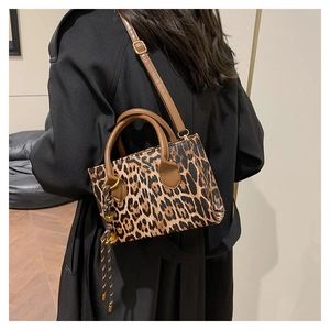 Chic leopard print handbag with brown handles worn with a long black winter coat