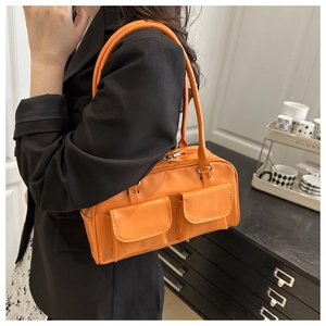 Side view of bright orange glossy shoulder bag with dual pockets on black blazer