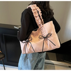 Detailed side view of pink nylon tote bag with black bows and pleated shoulder strap