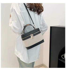 Detail of canvas box crossbody bag with black leather trim and dual gold zippers
