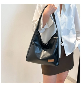 Detail of black PU leather hobo tote bag featuring a front pocket and brown logo patch